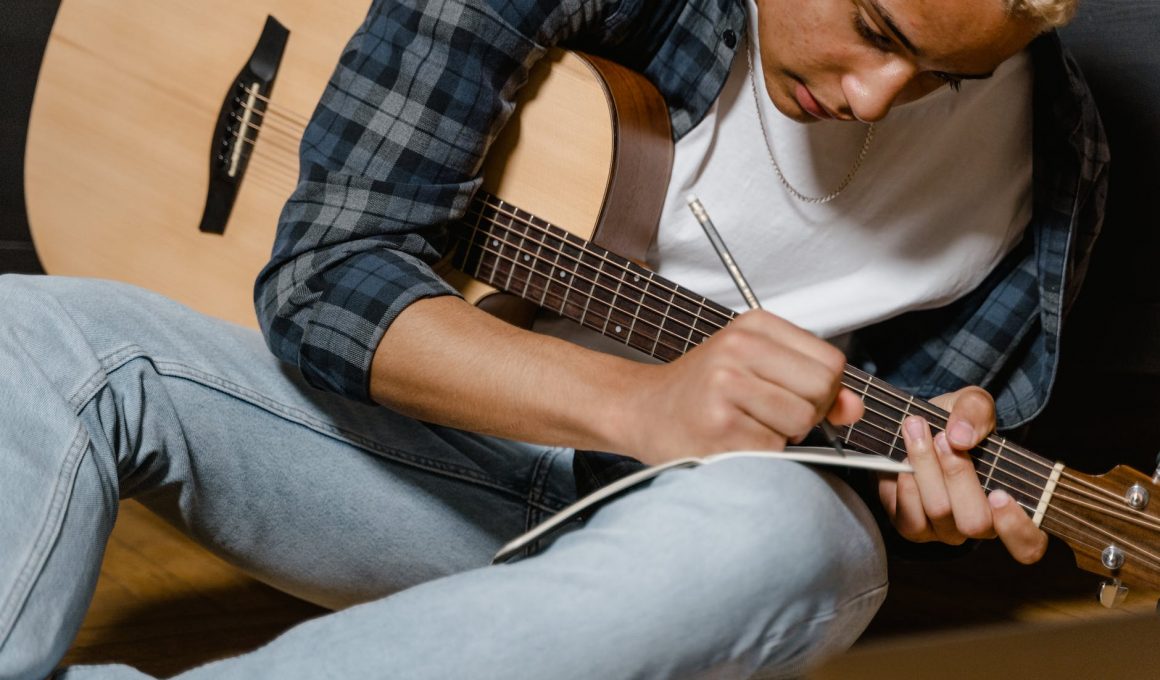 man in white shirt with a guitar writing a song
