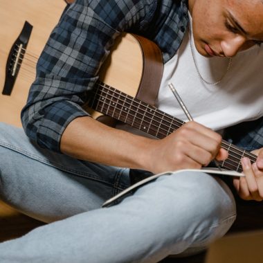 man in white shirt with a guitar writing a song