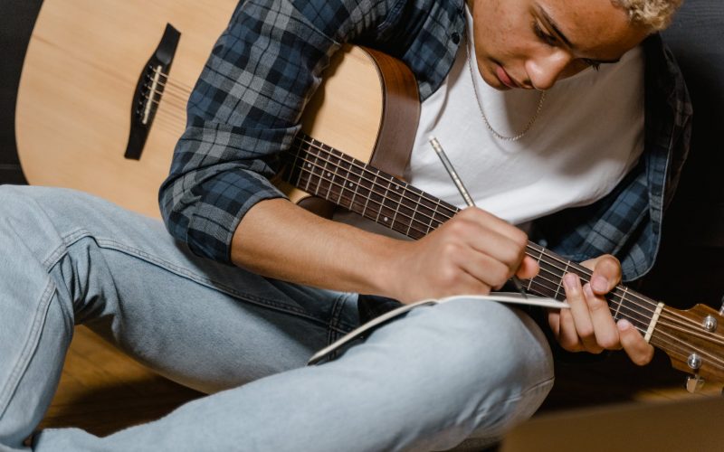 man in white shirt with a guitar writing a song